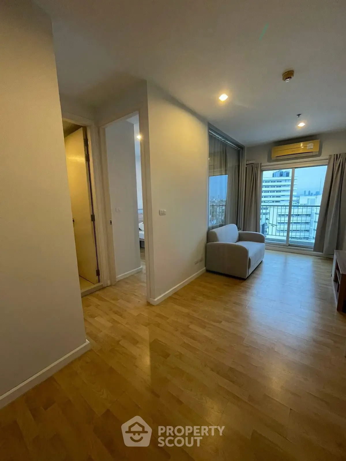 Spacious living room with wooden flooring and city view balcony in modern apartment.