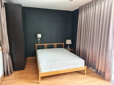 Spacious bedroom with wooden flooring and elegant curtains, featuring a comfortable bed and stylish lamps.