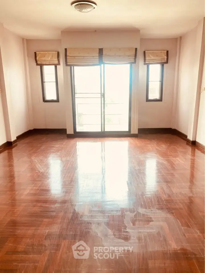 Spacious sunlit room with polished wooden floors and large windows.