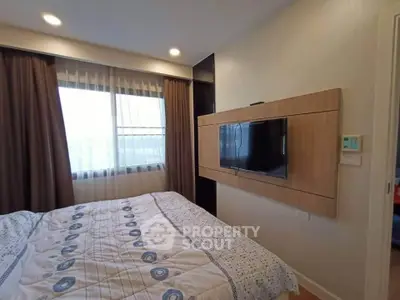 Cozy bedroom with modern TV setup and large window for natural light.