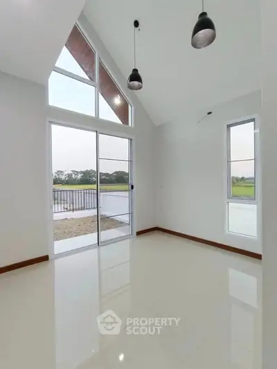 Spacious modern room with large windows and high ceiling, overlooking serene outdoor view.