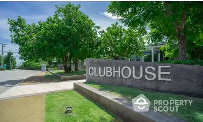 Modern clubhouse entrance surrounded by lush greenery and clear blue sky.