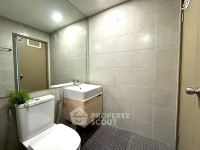 Modern bathroom with sleek fixtures and neutral tiles, featuring a compact vanity and toilet.