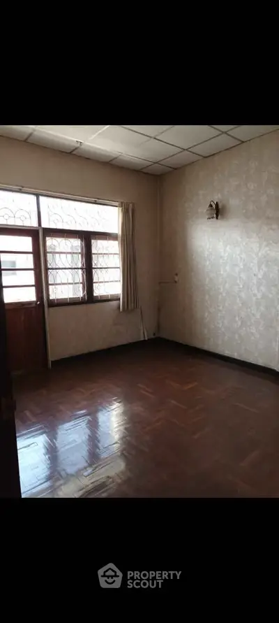 Spacious empty room with polished wooden floors and large window.