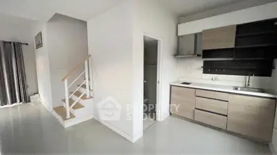 Modern open-layout kitchen with sleek cabinetry and adjacent staircase in a bright interior.