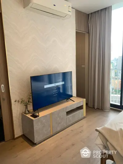 Modern bedroom with TV and city view, featuring stylish decor and natural light.