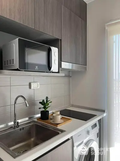 Modern kitchen with sleek cabinetry, microwave, and washing machine in compact layout.