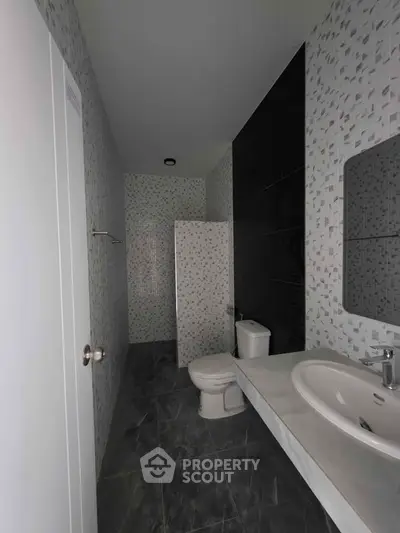 Modern bathroom with sleek design and tiled walls, featuring a sink, toilet, and shower area.
