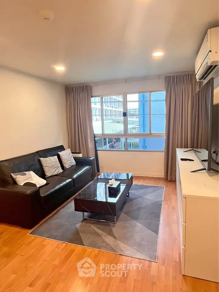 Modern living room with sleek furniture and large window offering city views.