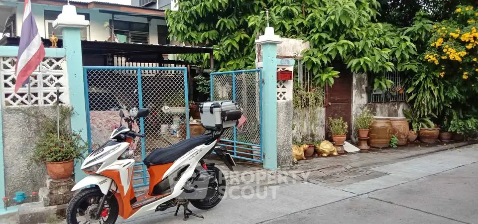 Charming residential entrance with lush greenery and scooter parked outside.