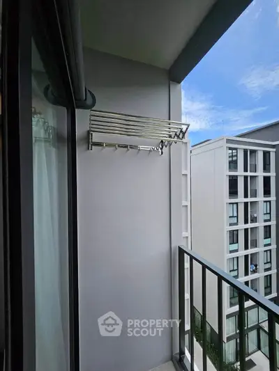 Modern apartment balcony with sleek railing and clothes drying rack, offering a view of neighboring buildings.