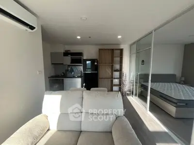 Modern open-plan living room with kitchen and bedroom, featuring sleek furniture and ample natural light.