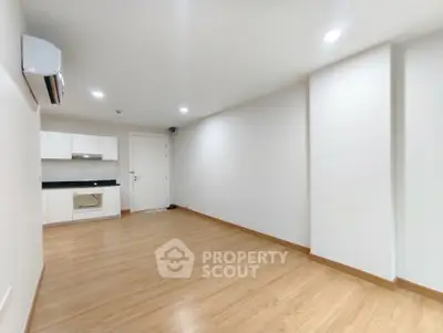 Spacious modern living room with wooden flooring and minimalist kitchen area.