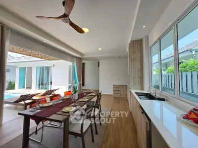 Spacious open-plan living area with dining table, modern kitchen, and poolside view in a luxury home.