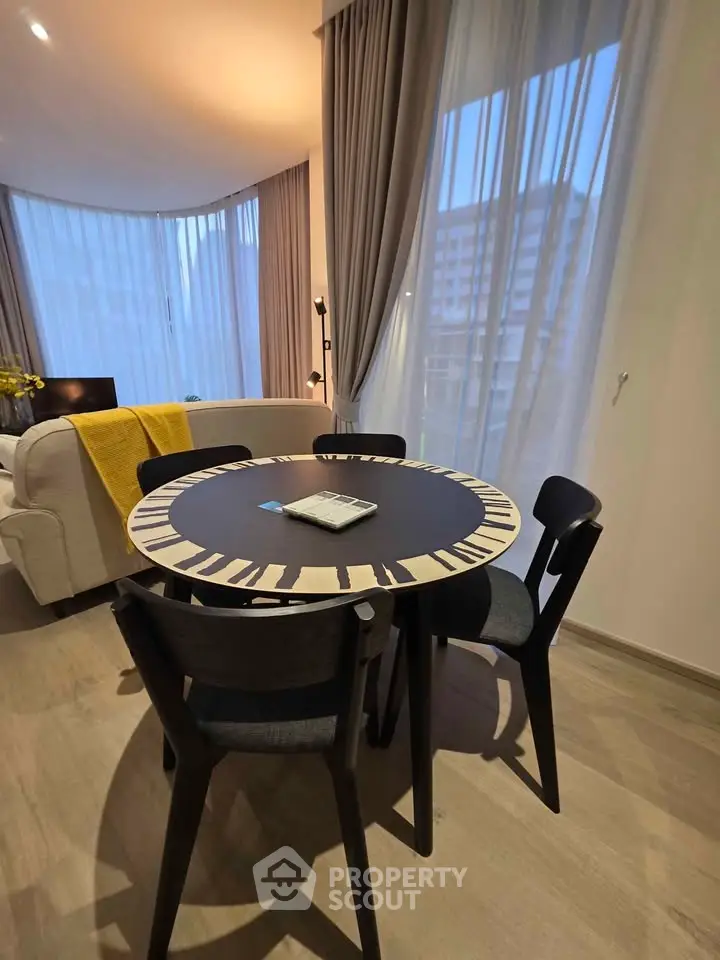 Modern living room with stylish round dining table and cozy seating area, featuring floor-to-ceiling windows.