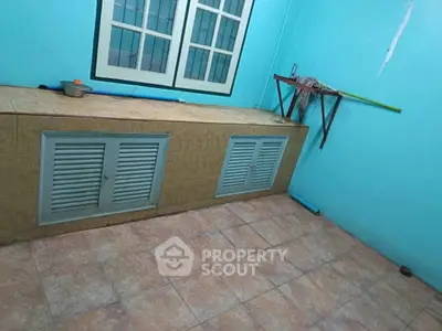 Simple room with tiled floor and blue walls, featuring a window and storage cabinets.