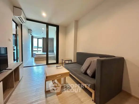 Modern living room with sleek furniture and glass partition leading to bedroom