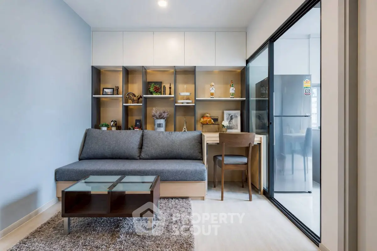 Modern living room with stylish furniture and glass partition leading to kitchen.