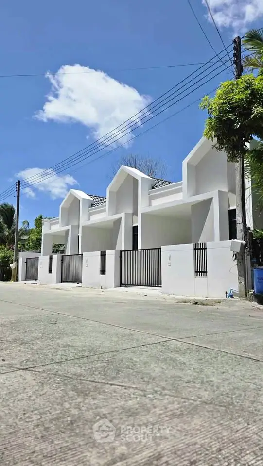 Modern white townhouses with unique roof design and gated entrance under a clear blue sky.