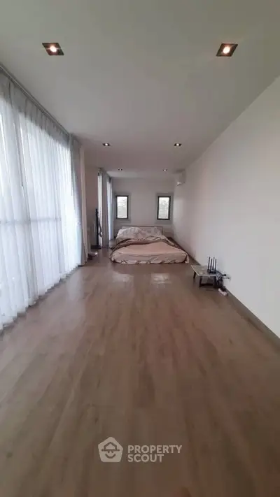 Spacious minimalist bedroom with wooden flooring and large windows for natural light.