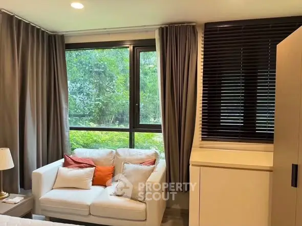 Cozy living room with large window and elegant curtains, featuring a comfortable white sofa and lush greenery view.