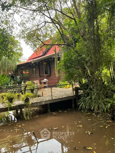 Charming rustic house with red roof nestled in lush greenery by a tranquil pond, perfect for nature lovers.