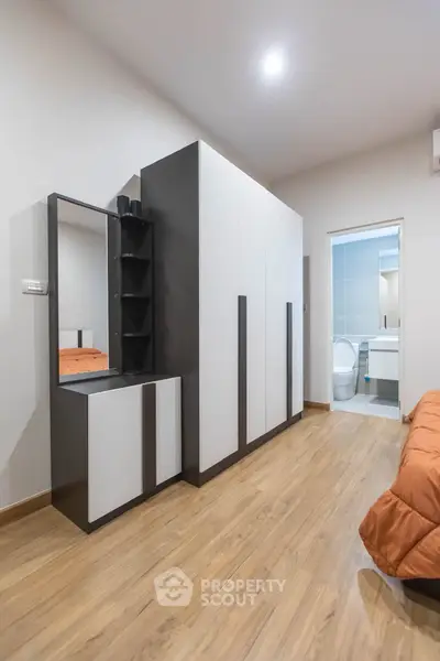 Modern bedroom with sleek wardrobe and ensuite bathroom, featuring wooden flooring and contemporary design.