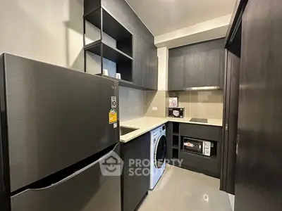 Modern kitchen with sleek dark cabinetry, fridge, and washing machine for efficient living.