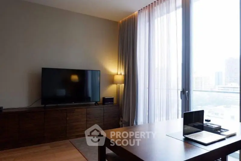 Modern living room with large TV and desk, featuring floor-to-ceiling windows and elegant curtains.