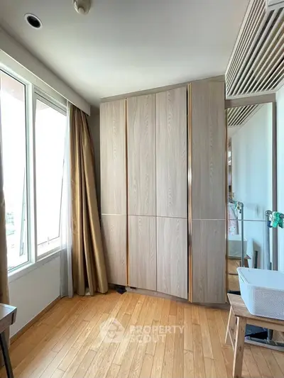 Bright bedroom with wooden flooring and large wardrobe, featuring natural light from a big window.