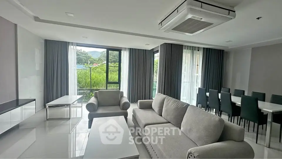 Spacious modern living room with large windows and elegant furniture, offering a serene view of lush greenery.