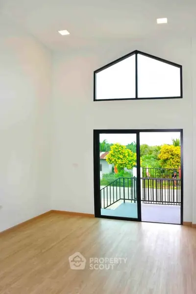 Spacious room with high ceiling and large window leading to a balcony with scenic views.