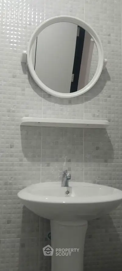 Modern bathroom with round mirror and sleek white sink in stylish tiled setting.