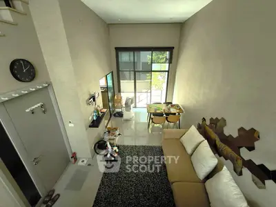 Modern living room with high ceiling and stylish decor, featuring a cozy sofa and dining area with natural light.