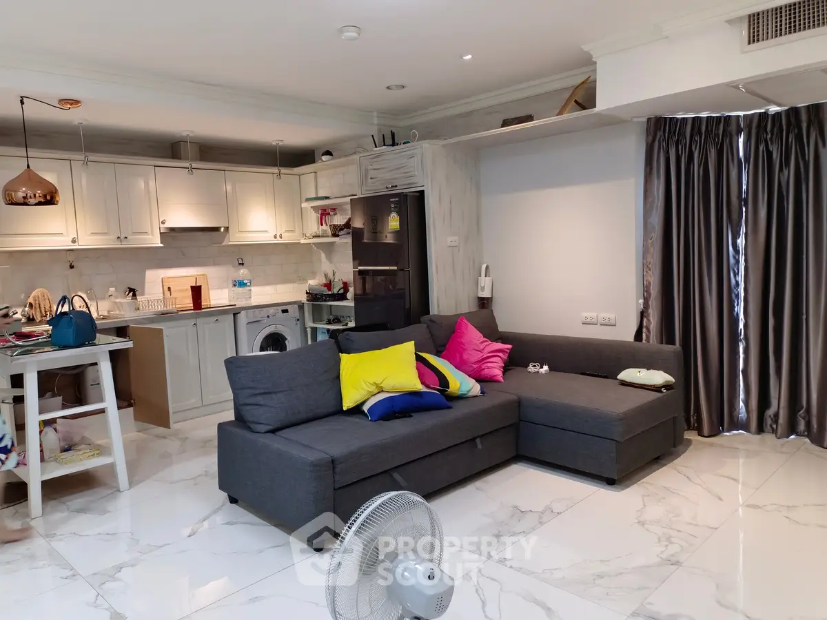 Modern living room with open kitchen, featuring stylish gray sofa and vibrant cushions, perfect for cozy gatherings.