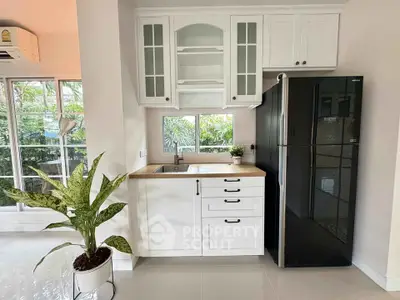 Charming kitchen with sleek black fridge and white cabinetry, overlooking lush greenery.