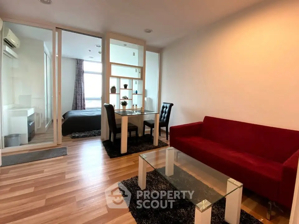 Modern living room with red sofa, glass table, and dining area in open-plan apartment.