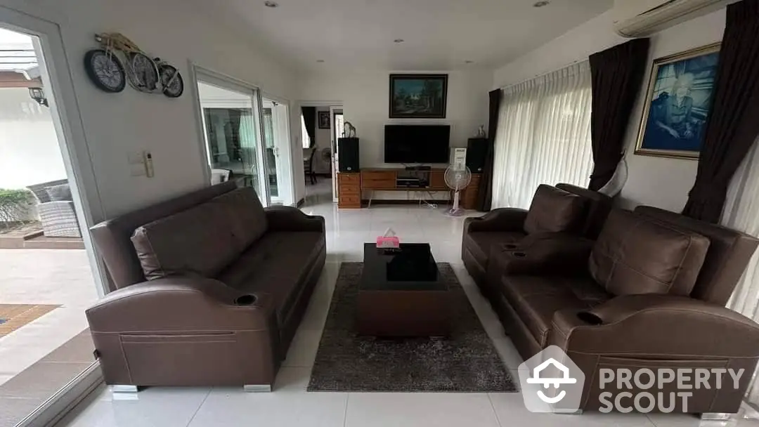 Spacious living room with large brown leather sofas, tiled flooring, and ample natural light, perfect for family gatherings.