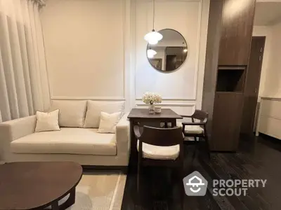 Elegant living space with a modern beige sofa, sleek wooden dining set, and a stylish round mirror, complemented by rich dark flooring and soft lighting.