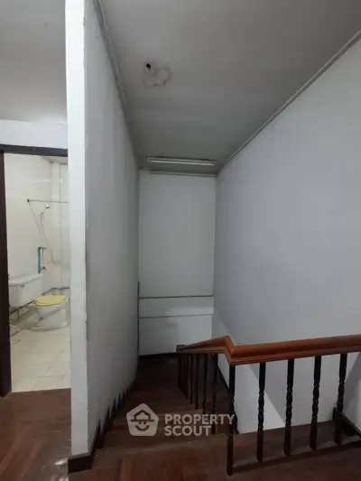 Staircase leading to a bathroom with wooden railing and white walls.