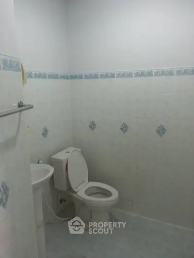 Simple bathroom with toilet and sink, tiled walls and floor, ideal for budget-friendly homes.