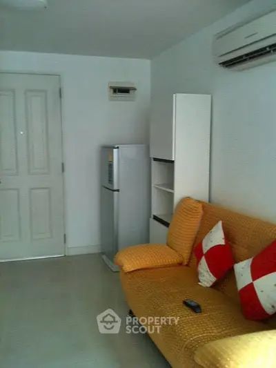 Cozy living room with orange sofa, air conditioning, and compact fridge.