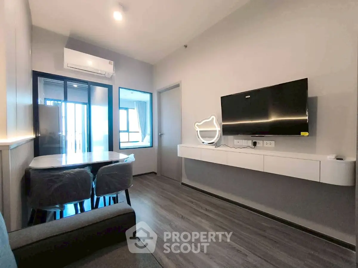 Modern living room with sleek furniture and wall-mounted TV, featuring a cozy dining area and balcony access.