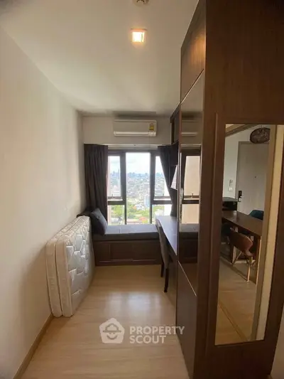 Compact bedroom with city view, featuring a window seat and air conditioning.