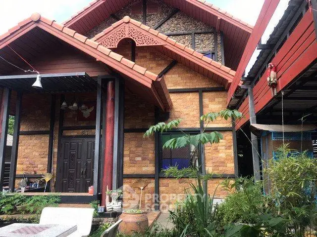 Charming rustic house with red roof and stone facade surrounded by lush greenery.