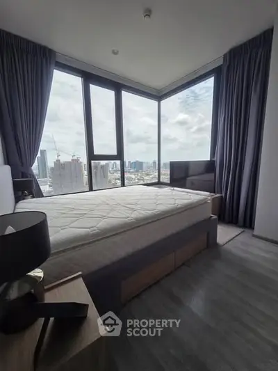Modern bedroom with large windows offering stunning city views, featuring a comfortable bed and stylish decor.