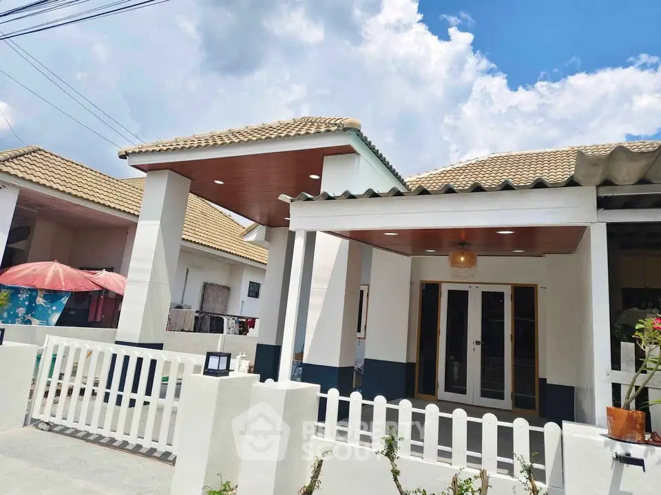 Charming single-story home with tiled roof and white picket fence under a bright blue sky.