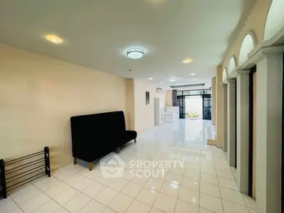 Spacious living room with modern lighting and tiled flooring, featuring a sleek black sofa and large windows.