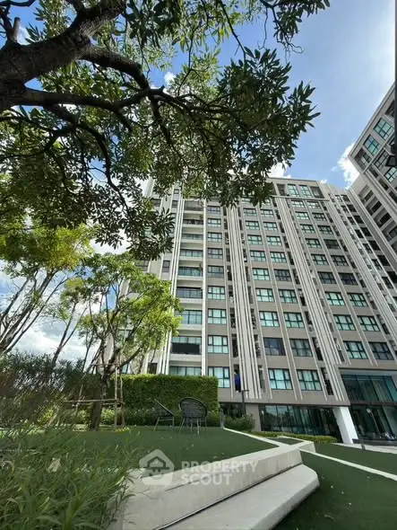 Modern high-rise building with lush garden and clear blue sky, perfect for urban living.