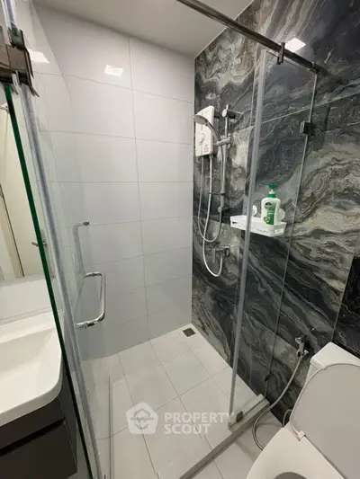 Modern bathroom with glass shower enclosure and stylish marble wall tiles.